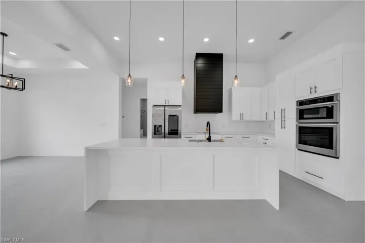 Kitchen with white cabinets, recessed lighting, appliances with stainless steel finishes, pendant lighting, and light stone countertops