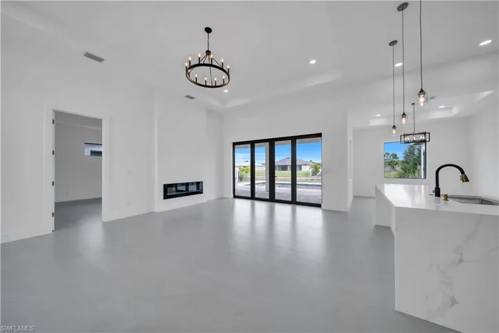 Unfurnished living room featuring a chandelier, a raised ceiling, concrete floors, a glass covered fireplace, and recessed lighting