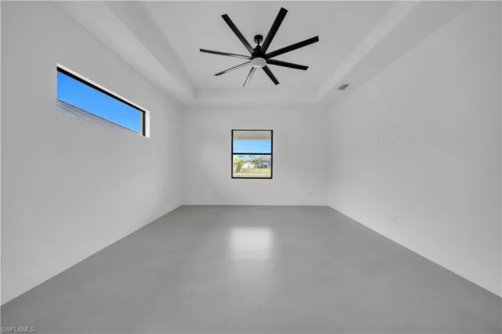 Empty room featuring a raised ceiling, plenty of natural light, finished concrete floors, and a ceiling fan