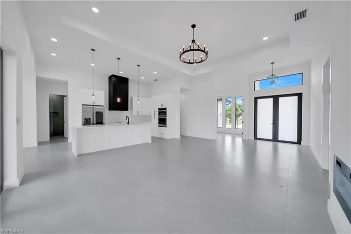 Unfurnished living room featuring a raised ceiling, french doors, a chandelier, a high ceiling, and recessed lighting