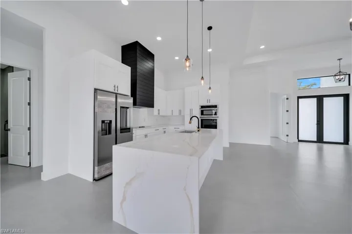 Kitchen with light stone countertops, appliances with stainless steel finishes, white cabinets, an island with sink, and hanging light fixtures