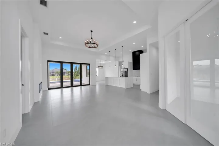 Unfurnished living room with a tray ceiling, concrete floors, a chandelier, and recessed lighting