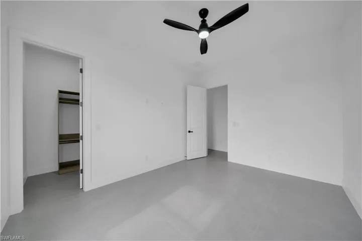 Unfurnished bedroom featuring a spacious closet, a ceiling fan, and finished concrete floors