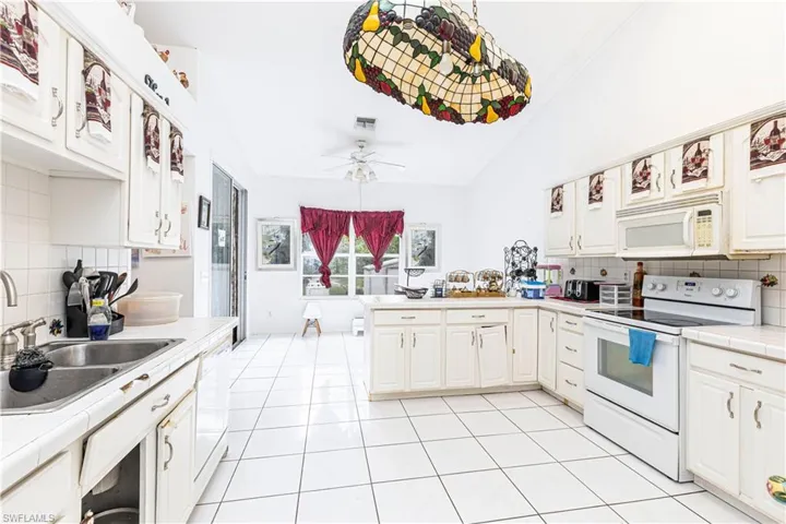Kitchen with white appliances, tile counters, a sink, backsplash, and lofted ceiling