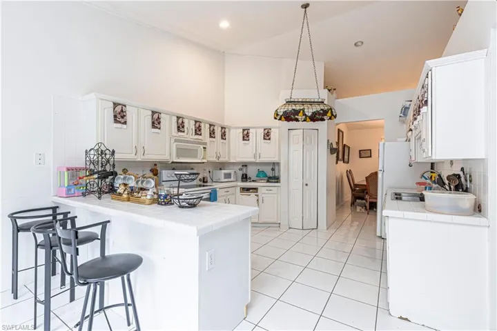 Kitchen with white appliances, tile countertops, a peninsula, high vaulted ceiling, and tasteful backsplash