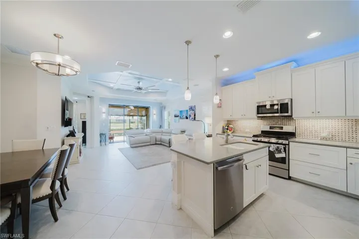 Kitchen with decorative light fixtures, stainless steel appliances, open floor plan, white cabinets, and an island with sink