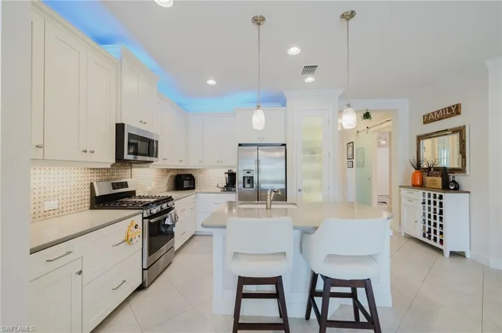 Kitchen with stainless steel appliances, white cabinets, a kitchen bar, backsplash, and recessed lighting