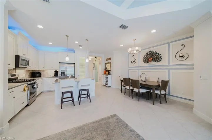 Kitchen with crown molding, stainless steel appliances, white cabinetry, hanging light fixtures, and a kitchen breakfast bar