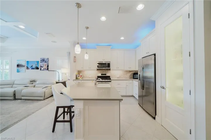 Kitchen with appliances with stainless steel finishes, pendant lighting, white cabinetry, decorative backsplash, and crown molding