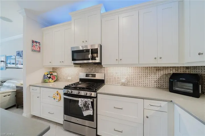 Kitchen featuring stainless steel appliances, white cabinetry, decorative backsplash, ornamental molding, and light tile patterned floors