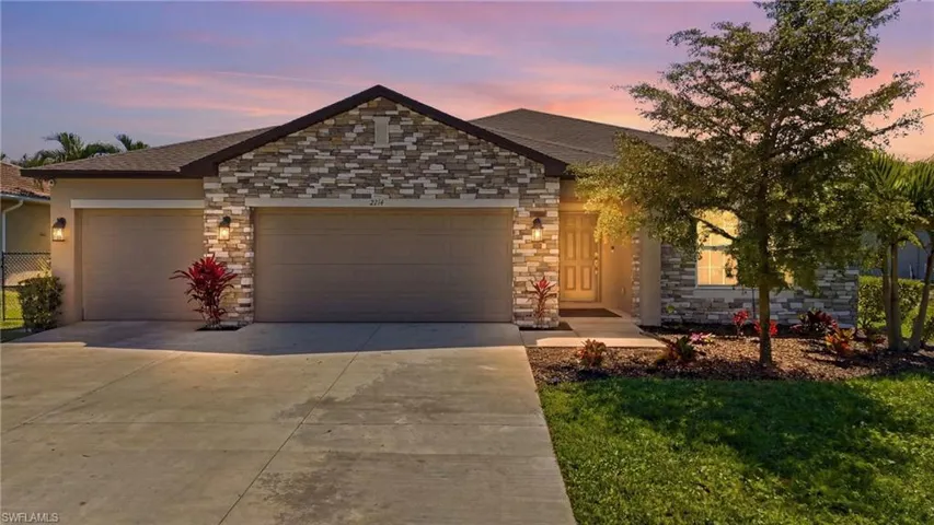View of front facade featuring stone siding, an attached garage, driveway, a shingled roof, and a lawn