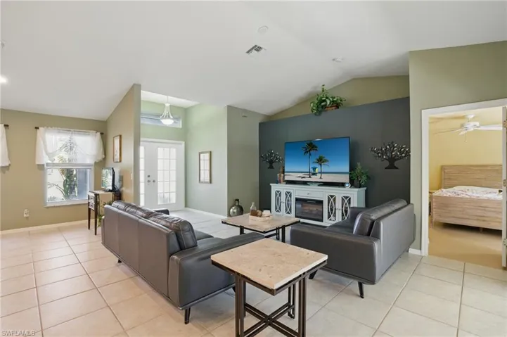 Living area featuring light tile patterned floors, a ceiling fan, baseboards, visible vents, and lofted ceiling