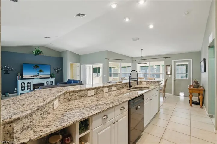 Kitchen featuring light stone countertops, dishwasher, vaulted ceiling, light tile patterned floors, and a sink