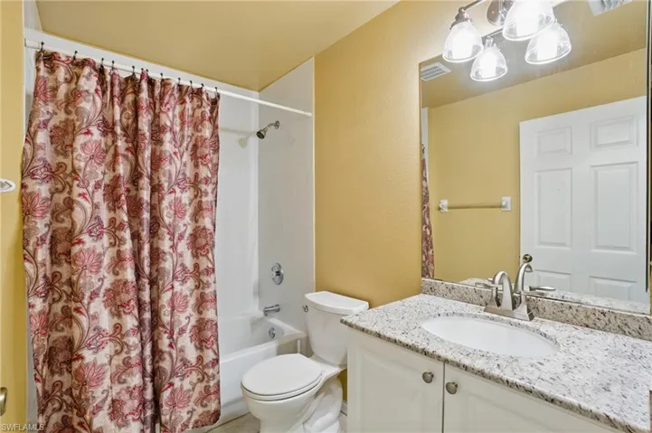 Full bath featuring visible vents, toilet, shower / bath combination with curtain, vanity, and a textured wall