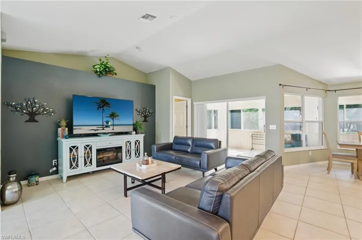Living area with light tile patterned floors, visible vents, baseboards, and vaulted ceiling