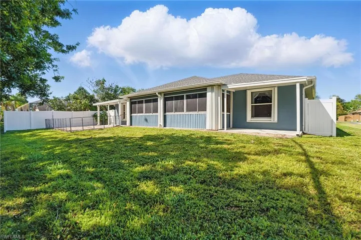 Rear view of house with a lawn, fence, a sunroom, and stucco siding