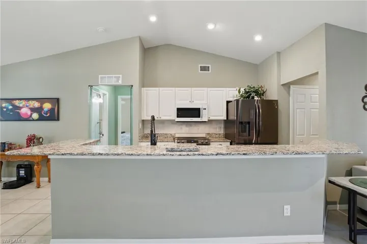 Kitchen with white microwave, visible vents, stainless steel refrigerator with ice dispenser, and light tile patterned floors