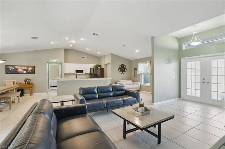 Living room with vaulted ceiling, light tile patterned flooring, french doors, and visible vents