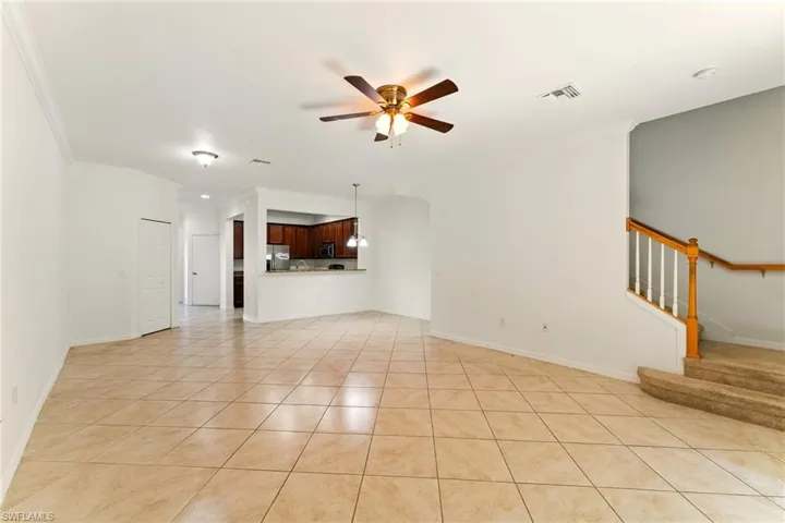 Unfurnished living room featuring ceiling fan, light tile patterned flooring, crown molding, stairs, and baseboards