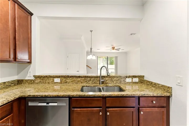 Kitchen with stainless steel dishwasher, a sink, dark brown cabinets, light stone counters, and a ceiling fan