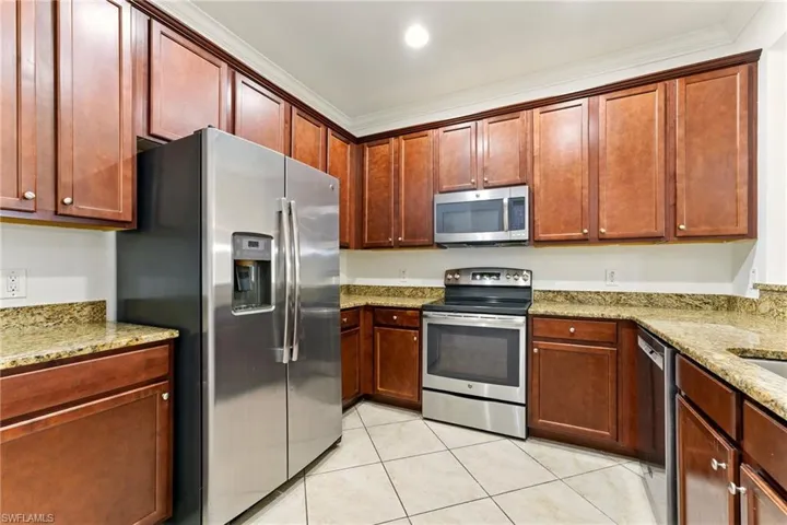 Kitchen featuring appliances with stainless steel finishes, light tile patterned floors, crown molding, light stone counters, and recessed lighting