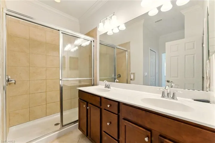 Full bathroom with a stall shower, double vanity, crown molding, and tile patterned floors