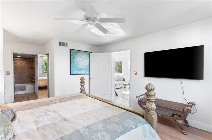 Primary bedroom features wood finished floors, ensuite bath and walk-in closet, ceiling fan, and wall-mounted TV