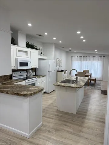Kitchen featuring white cabinetry, a kitchen island with sink, white appliances, recessed lighting, and light wood finished floors