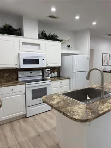 Kitchen featuring white appliances, white cabinetry, light wood-style floors, dark stone counters, and recessed lighting