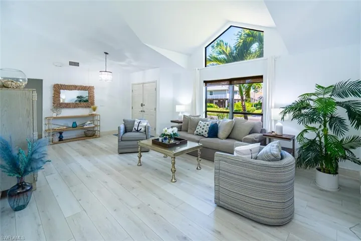 Living area with light wood-type flooring, a chandelier, and high vaulted ceiling