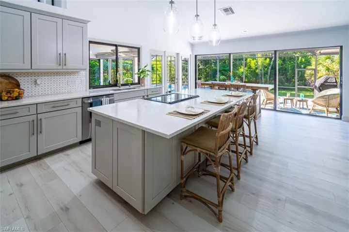 Kitchen featuring lofted ceiling, gray cabinetry, decorative backsplash, a kitchen island, and light wood-style floors
