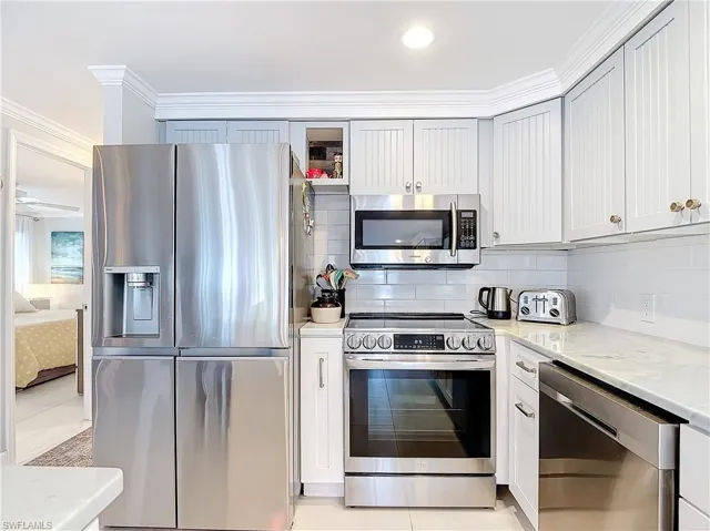 Kitchen featuring stainless steel appliances, light stone countertops, backsplash, glass insert cabinets, and ornamental molding