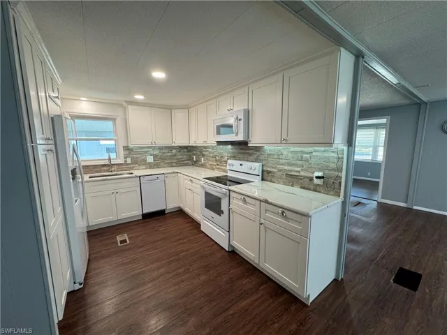 Kitchen with white cabinets, white appliances, dark wood-type flooring, a textured ceiling, and quartz countertops