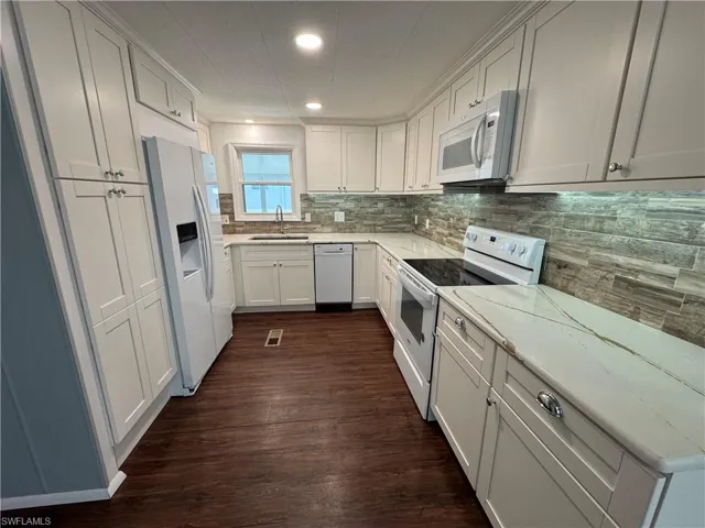Kitchen featuring white appliances, white cabinetry, dark wood-type flooring, quartz counters, and tile backsplash