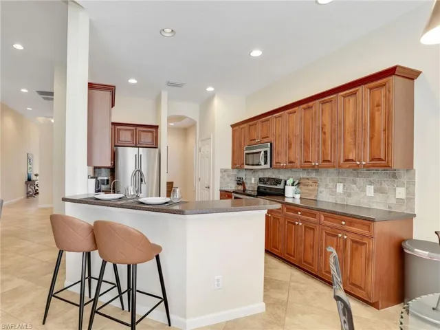 Kitchen with stainless steel appliances, dark countertops, arched walkways, backsplash, and recessed lighting