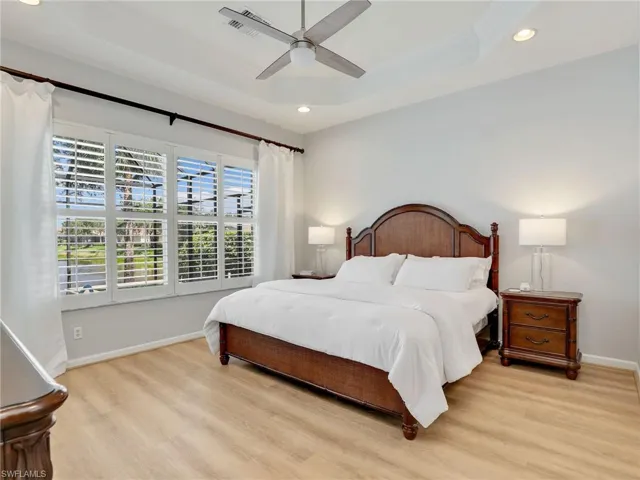 Bedroom with a tray ceiling, recessed lighting, light wood-style flooring, baseboards, and ceiling fan