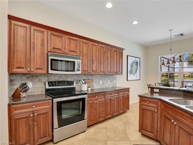 Kitchen featuring appliances with stainless steel finishes, decorative backsplash, brown cabinetry, light tile patterned flooring, and recessed lighting