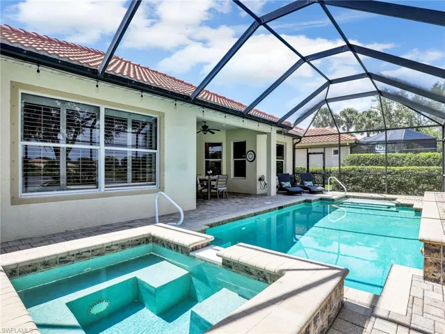 View of swimming pool featuring ceiling fan, a patio, a pool with connected hot tub, and glass enclosure