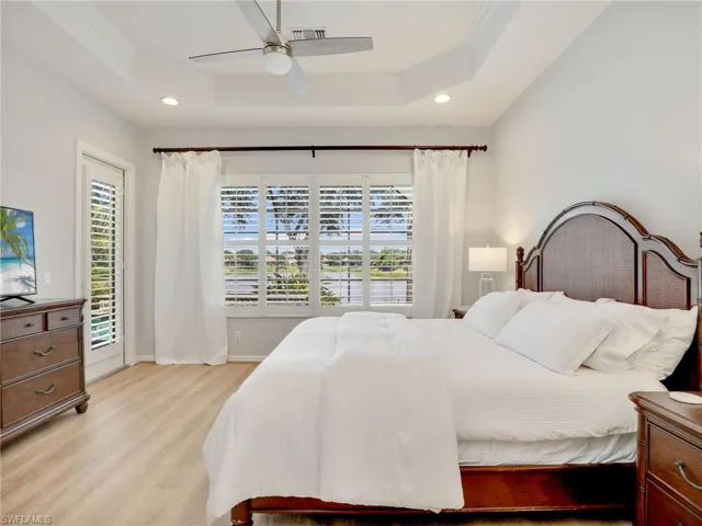 Bedroom with a tray ceiling, light wood finished floors, ornamental molding, recessed lighting, and baseboards