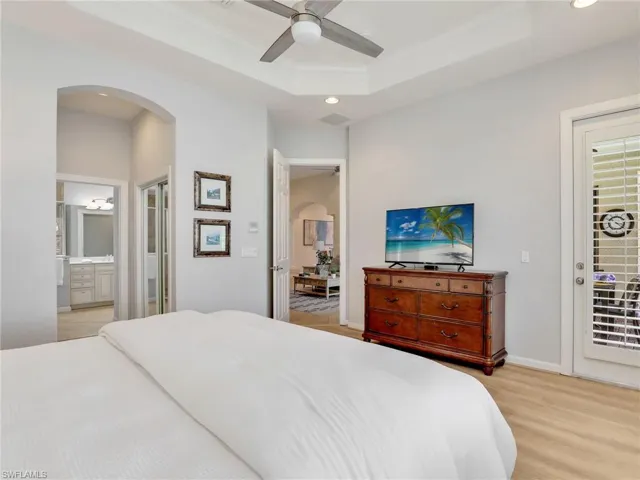 Bedroom featuring arched walkways, recessed lighting, ornamental molding, light wood-style flooring, and a tray ceiling