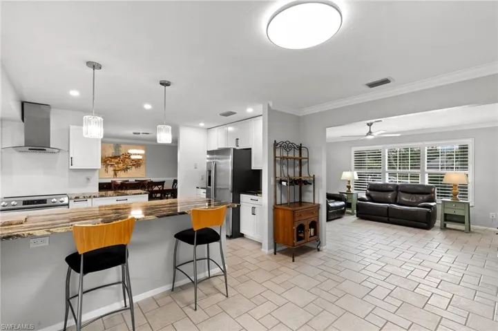 Kitchen featuring white cabinetry, a kitchen breakfast bar, dark stone countertops, wall chimney range hood, and recessed lighting
