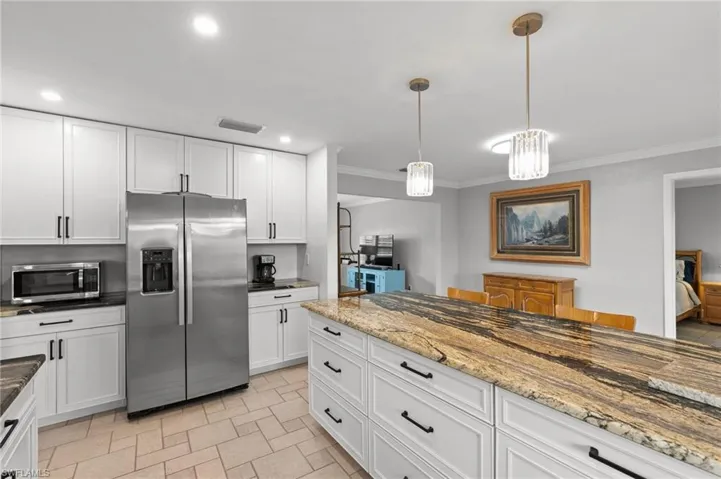 Kitchen featuring white cabinetry, dark stone counters, appliances with stainless steel finishes, hanging light fixtures, and crown molding