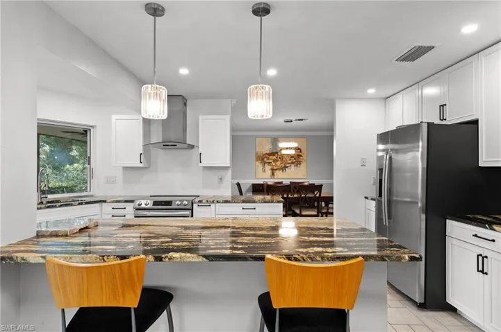 Kitchen with dark stone counters, a breakfast bar, wall chimney range hood, white cabinetry, and recessed lighting