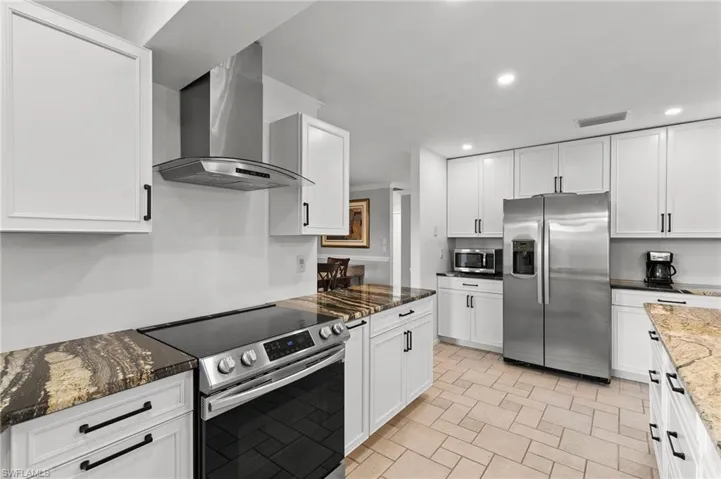 Kitchen featuring stainless steel appliances, wall chimney range hood, dark stone counters, recessed lighting, and white cabinetry