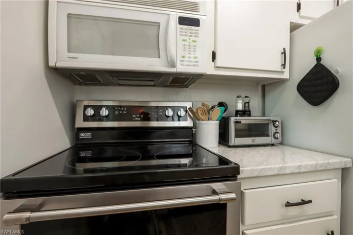 Kitchen featuring stainless steel range with electric stovetop, white microwave, tasteful backsplash, and white cabinetry