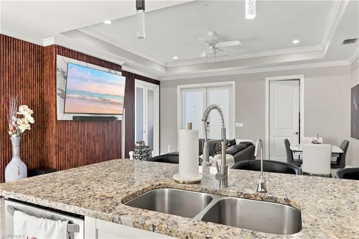 Kitchen featuring a stone-surface island with a double-basin stainless steel sink and high-arc faucet, complemented by a floor-to-ceiling slatted wood accent wall and a tray ceiling with recessed lighting