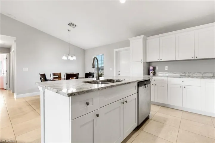 Kitchen with pendant lighting, dishwasher, white cabinets, sink, and an island with sink