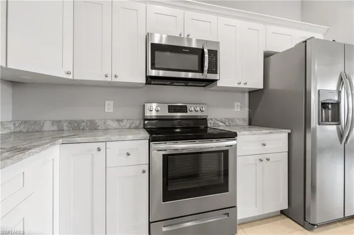 Kitchen featuring white cabinets, light stone countertops, stainless steel appliances, and light tile patterned floors