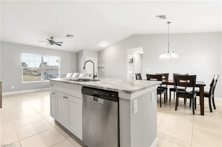 Kitchen featuring dishwasher, ceiling fan with notable chandelier, sink, hanging light fixtures, and an island with sink