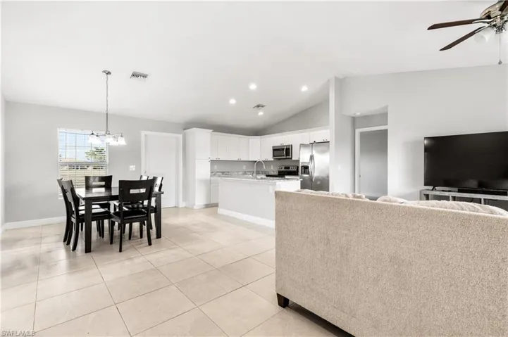 Kitchen with stainless steel appliances, vaulted ceiling, light tile patterned floors, decorative light fixtures, and white cabinetry